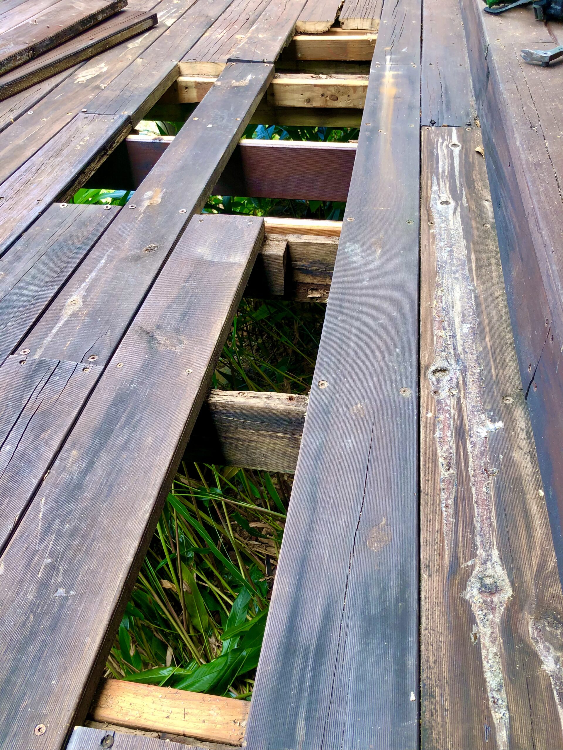 A partially dismantled wooden deck undergoing repairs, showing damaged planks and exposed framework. Handyman Port Douglas.
