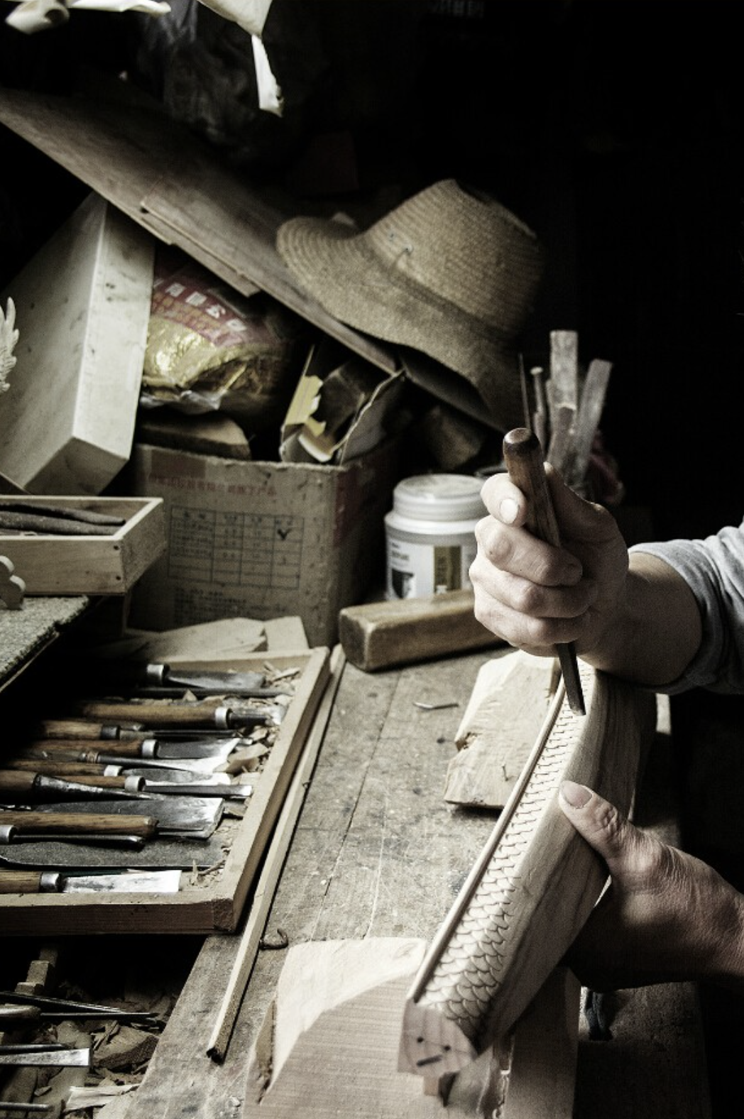 A craftsman hand-carving an intricate pattern into a wooden piece, surrounded by traditional woodworking tools in a rustic workshop.